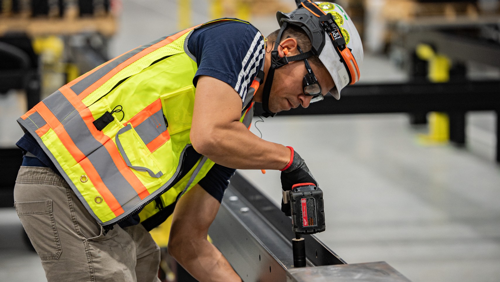 Accelevation technician in a hi-vis vest drilling a steel channel on the manufacturing floor