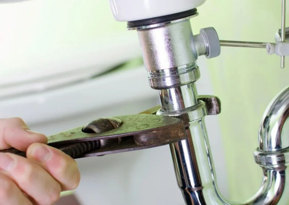 Hand using a wrench to tighten or loosen a pipe fitting under a sink.