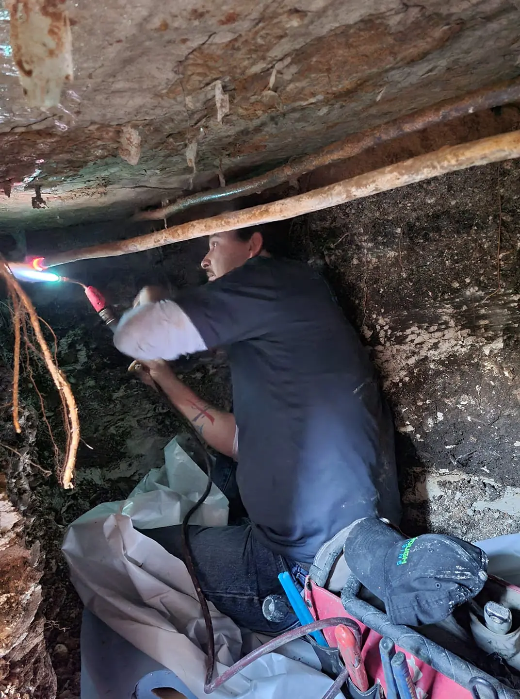 Worker using a torch to weld or repair a pipe in a narrow underground space.
