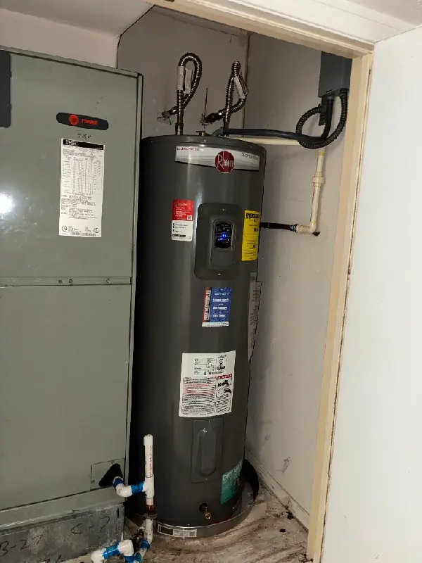 Gray Rheem water heater installed next to an electrical panel in a utility closet.
