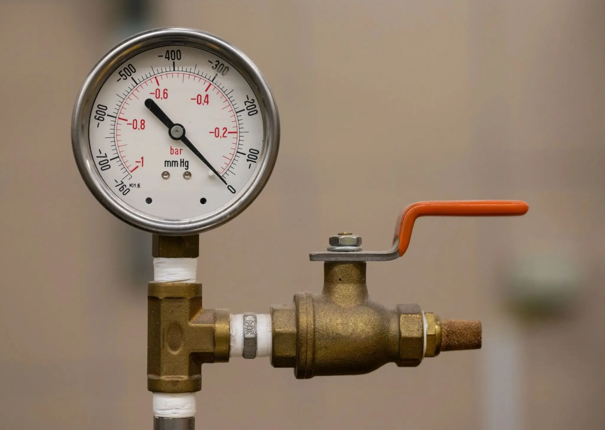 Pressure gauge and brass valve with orange handle on a pipe against a blurred background.