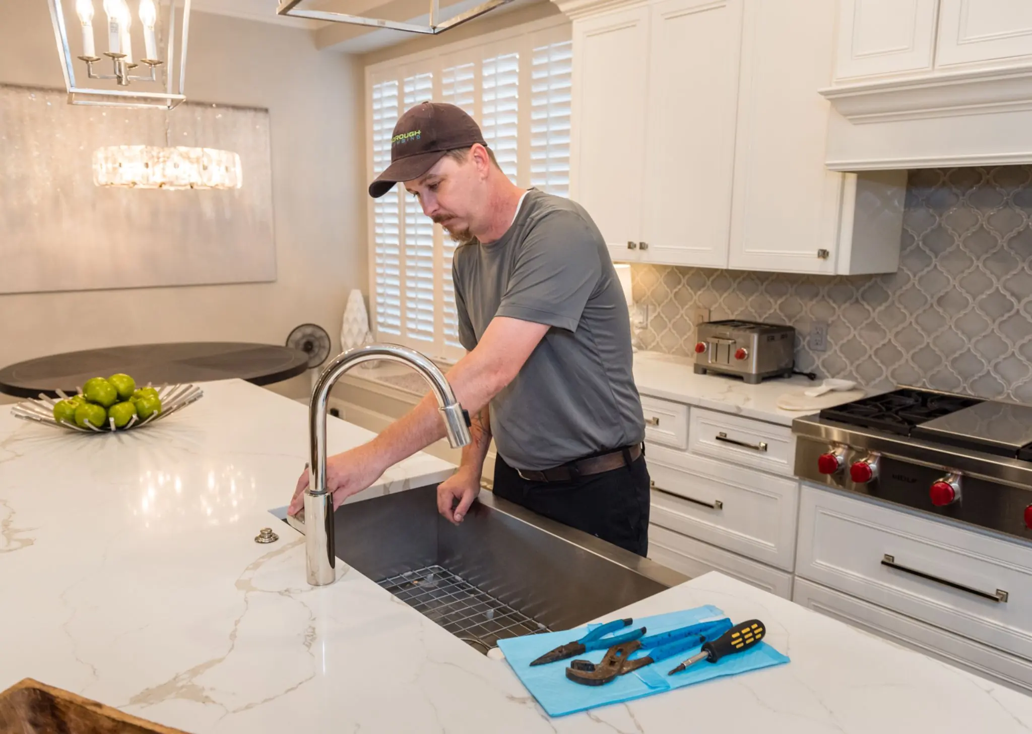 Plumber inspecting kitchen sink faucet with tools on countertop in a modern kitchen.
