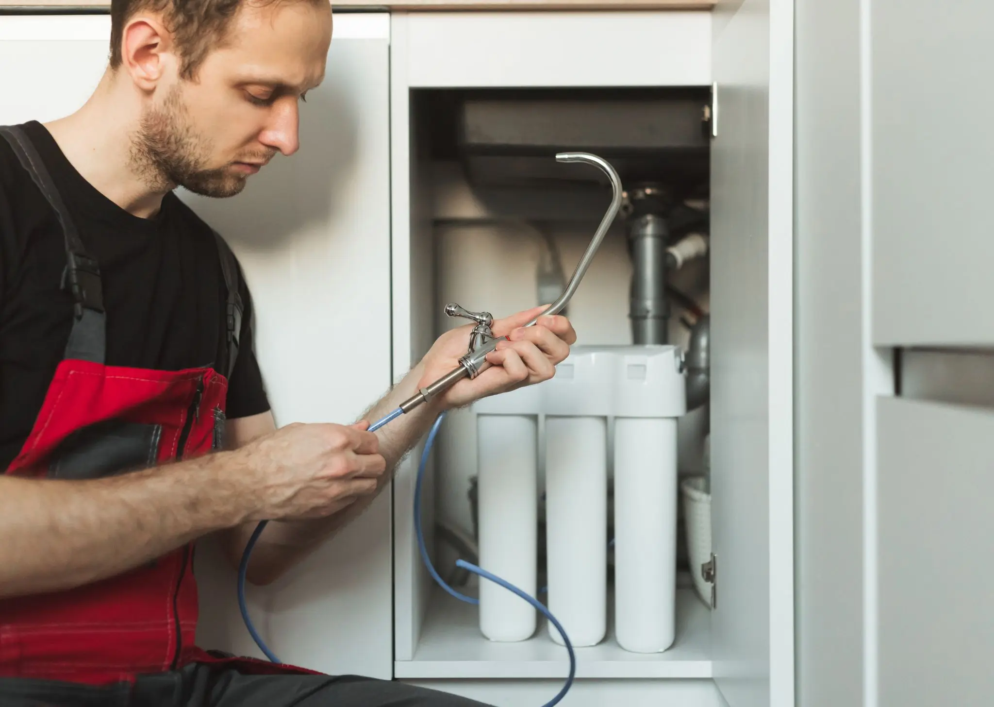 Technician installing or repairing a water filtration system under a kitchen sink.