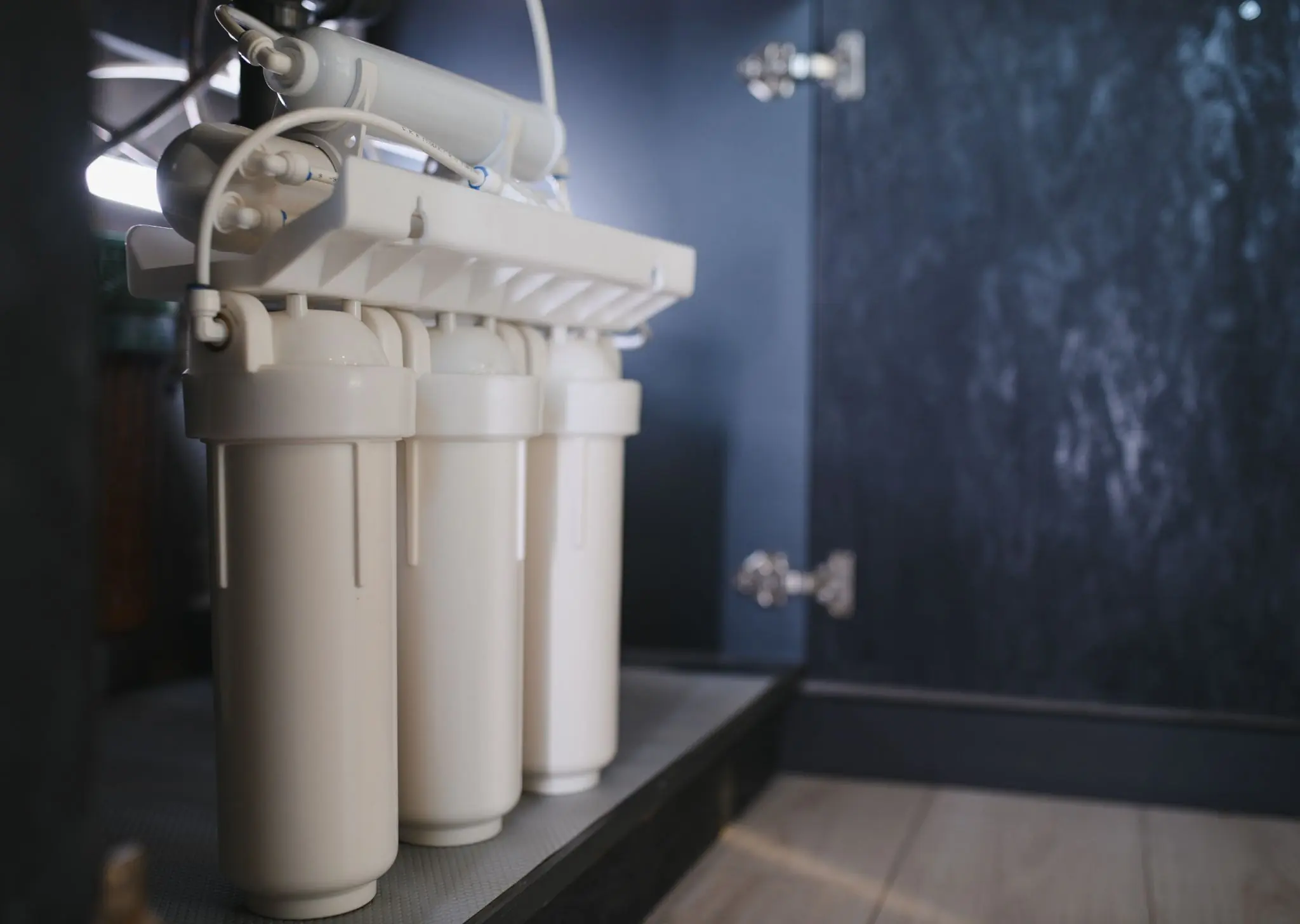 White water filtration system installed under a kitchen sink with pipes and connectors visible.