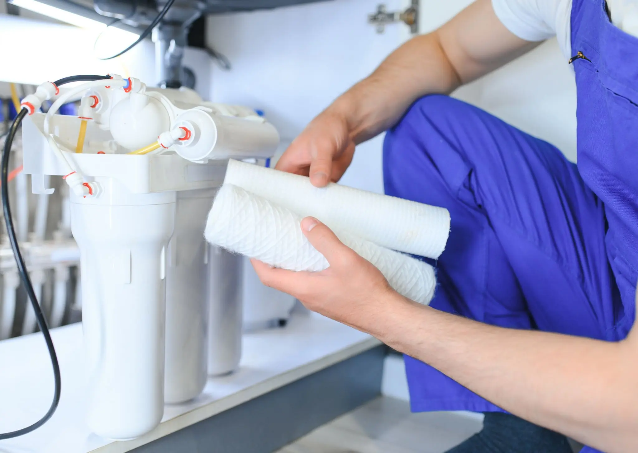 Technician in blue overalls installing or replacing filters in a white water filtration system.