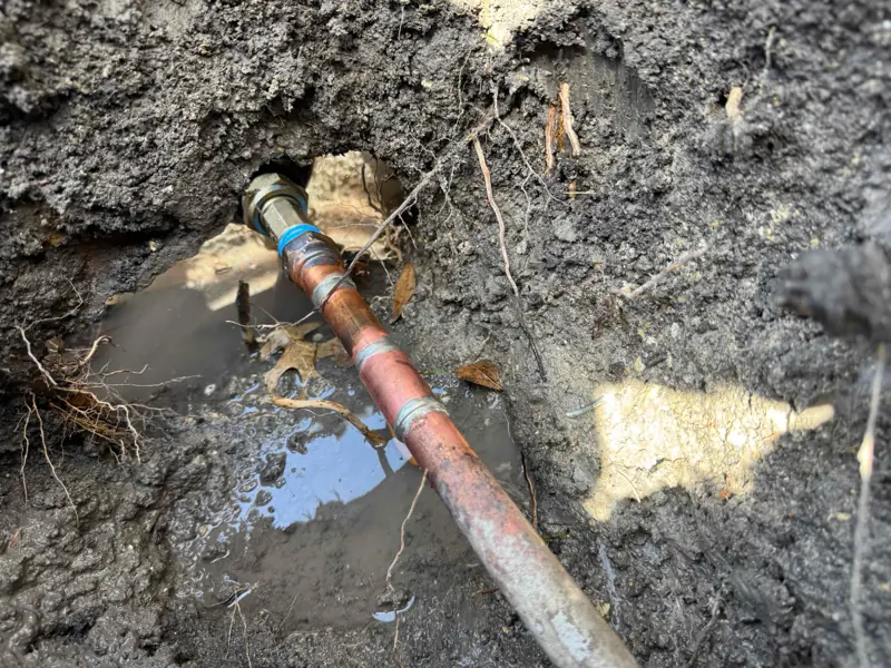 Exposed copper pipe with joints partially buried in muddy soil with some water around it.