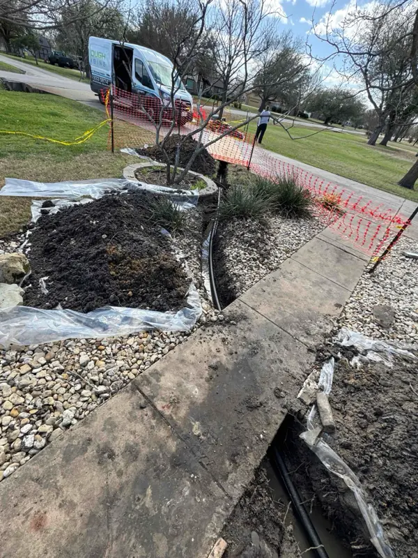 Outdoor trench water line repair near sidewalk with soil piles and a service van in the background.