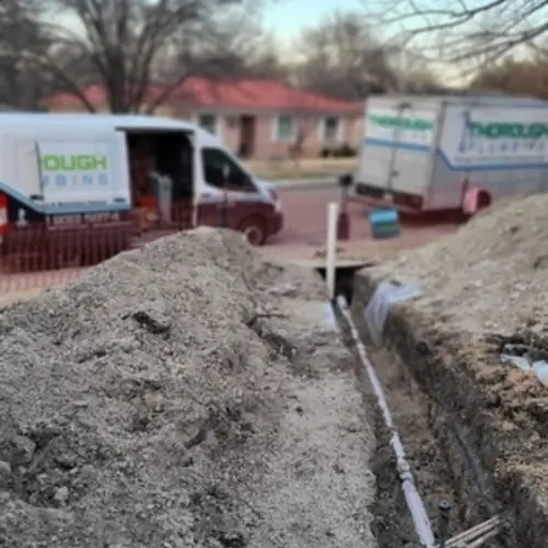 Trenched earth soil with exposed pipeline and two vans with business logos in the background.
