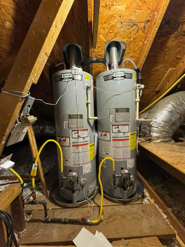 Gray water heater tank installed in a small corner space near a door and a light switch on a beige wall.