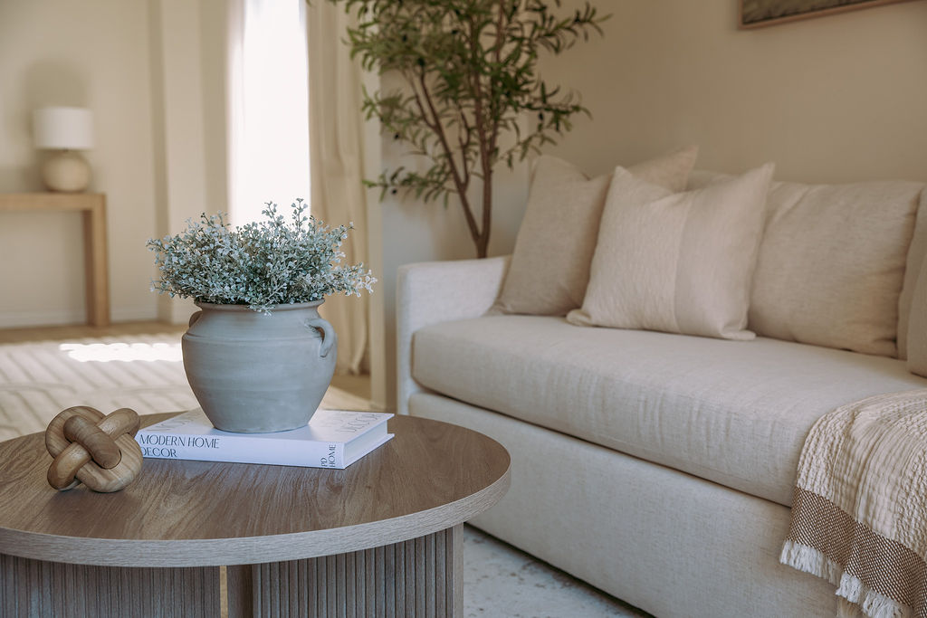 A modern dining room boasts an oval white table with wishbone chairs, a large round mirror above a woven buffet, and a vintage-style pendant light, all on a patterned rug.