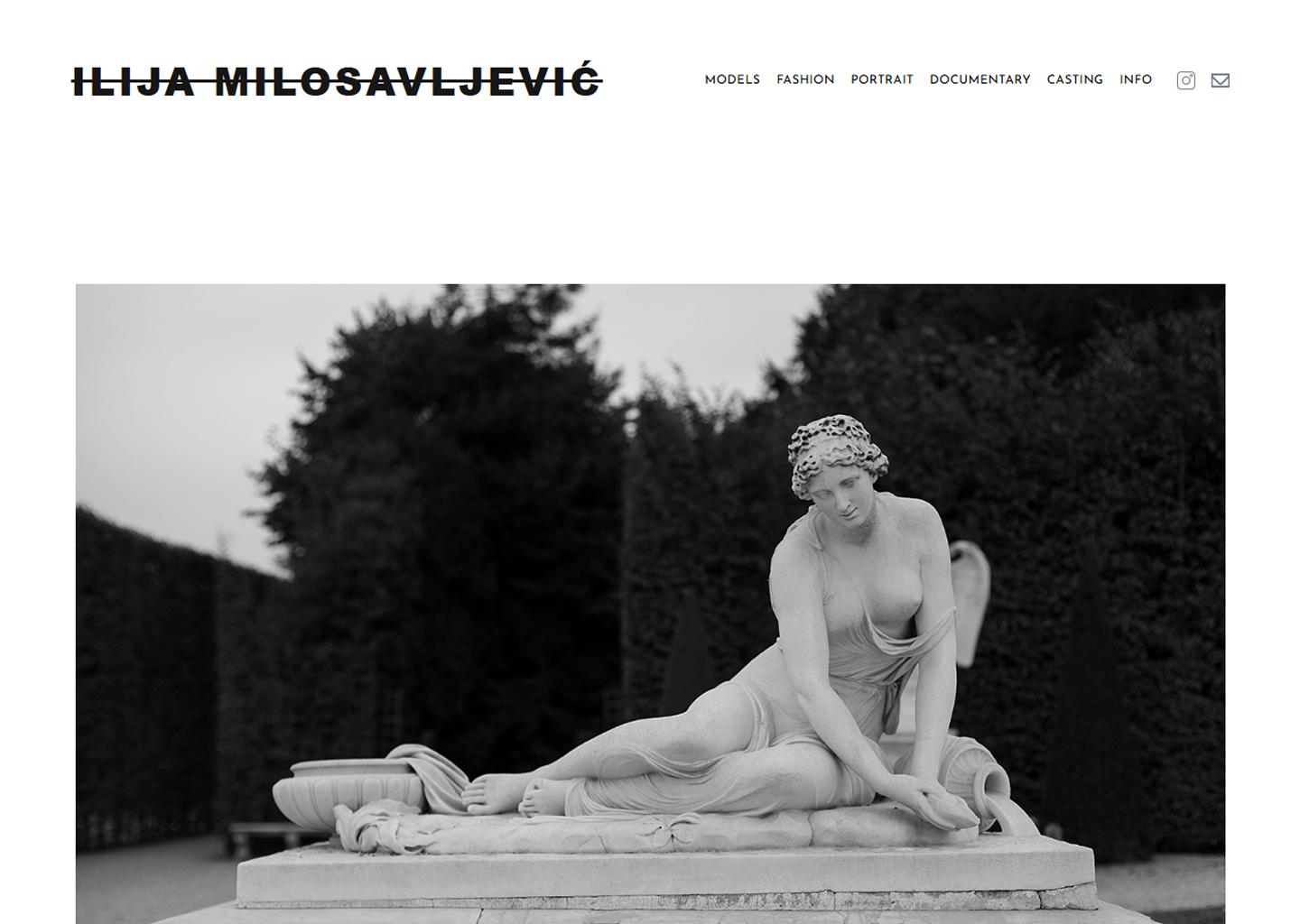 Black and white photo of a reclining classical statue of a woman with flowing hair and draped cloth.