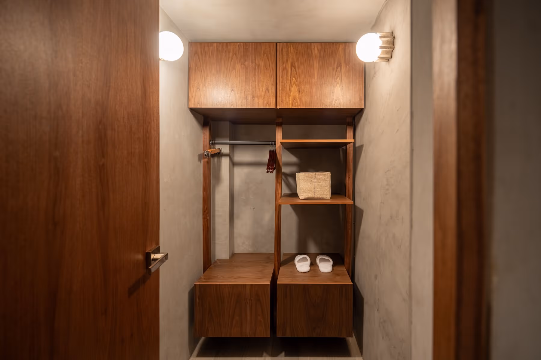 Small wooden closet with shelves, hanging rod, slippers, and folded towel inside.
