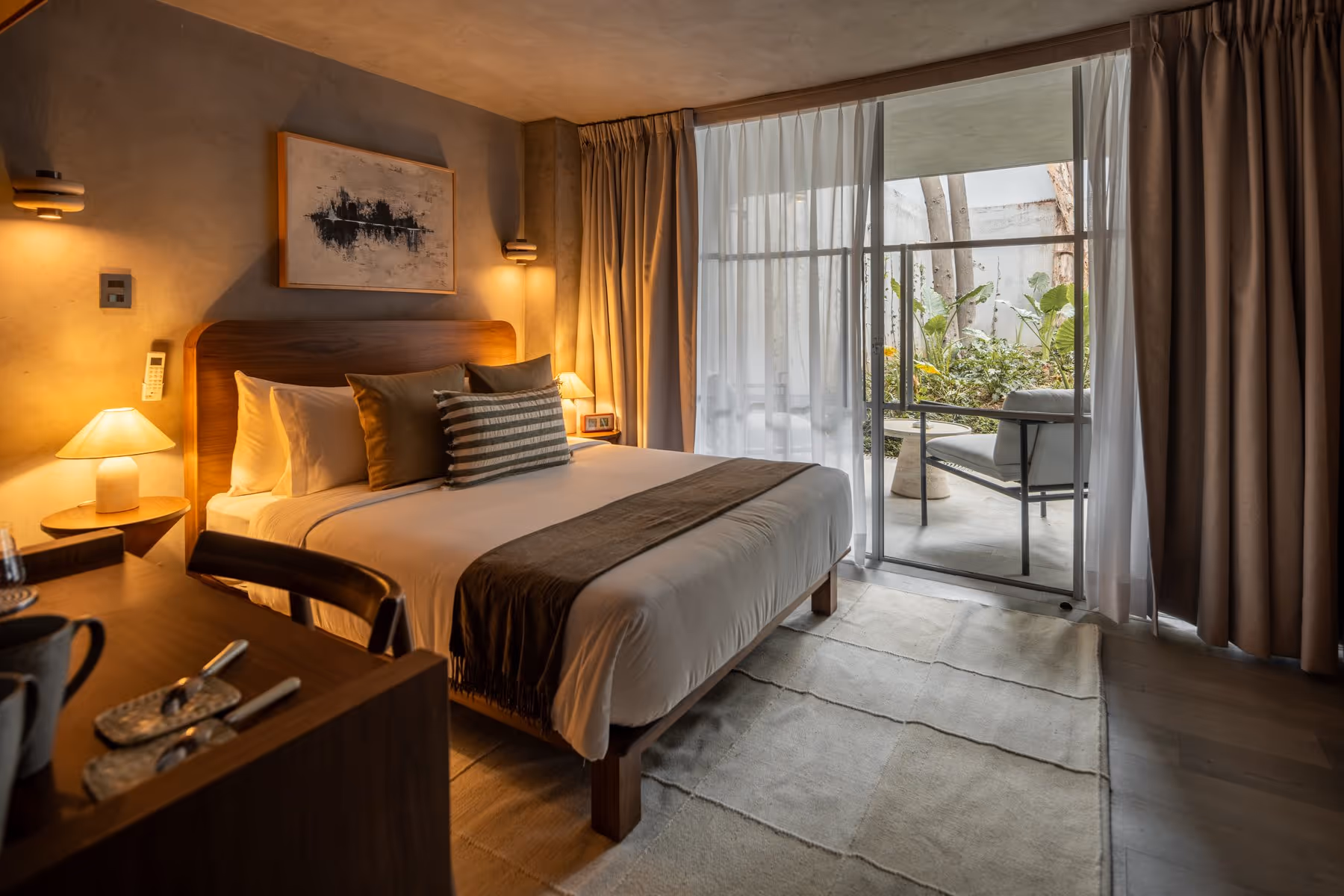 Cozy hotel room with a large bed, bedside lamps, curtains, and a balcony with outdoor seating.