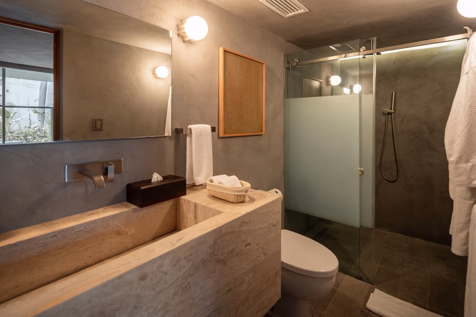 Modern bathroom with stone sink, wall-mounted faucet, towel, toilet, and shower with frosted glass door.