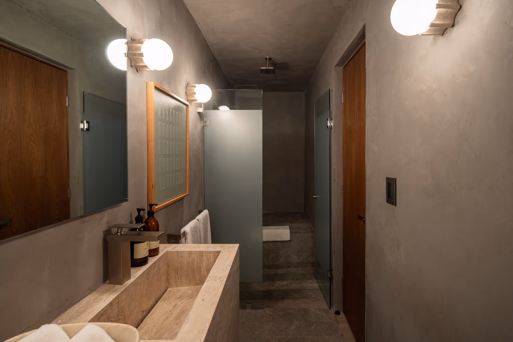 Modern bathroom with stone sink, towel rack, glass shower partition, and wooden doors on plaster walls.