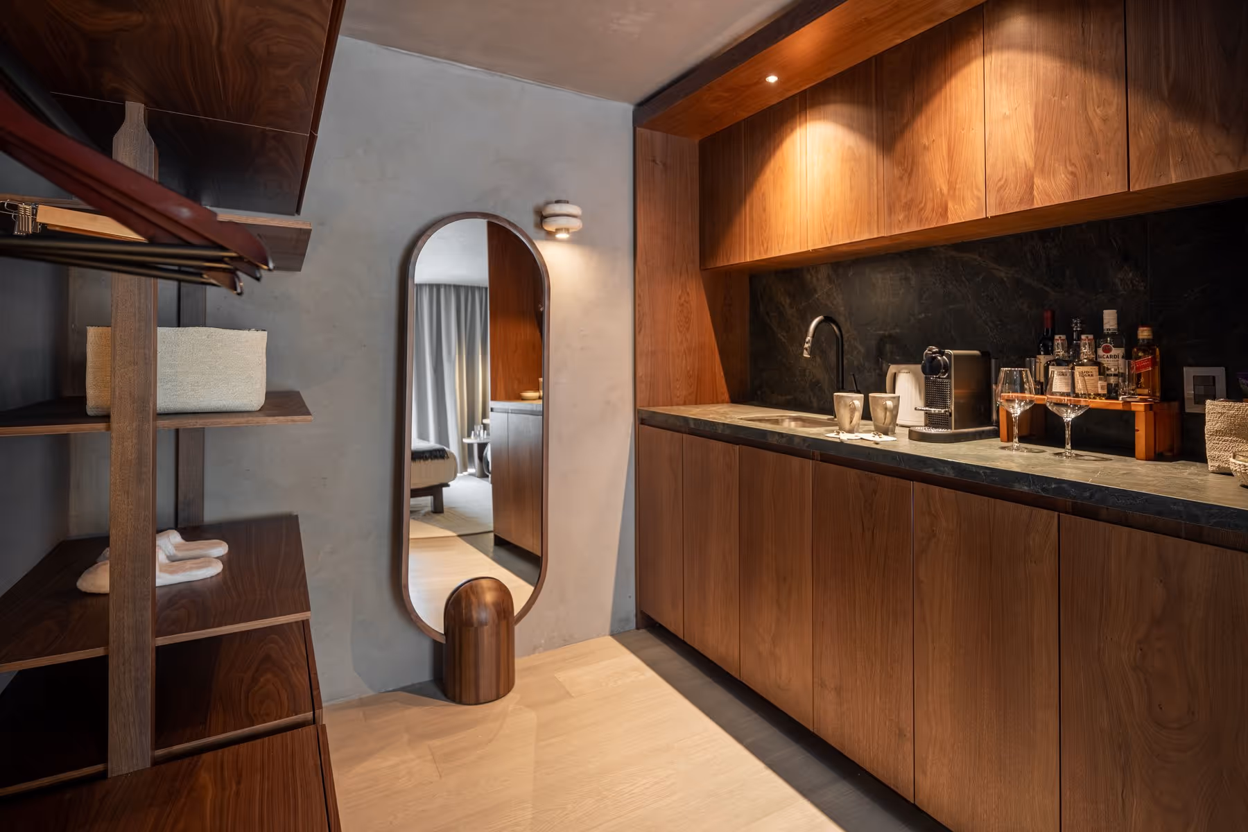 Modern room with wooden cabinets, a coffee machine, glasses, bottles, mirror, and open shelving.