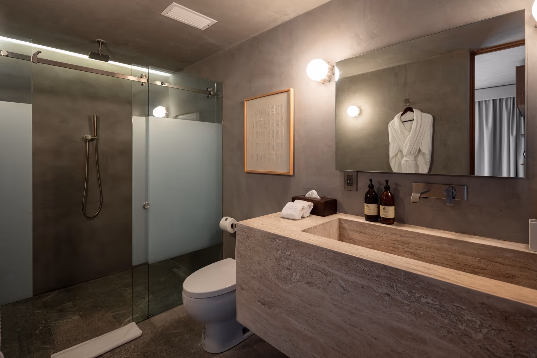 Modern bathroom with a stone sink, glass shower, toilet, mirror, and a white bathrobe hanging.