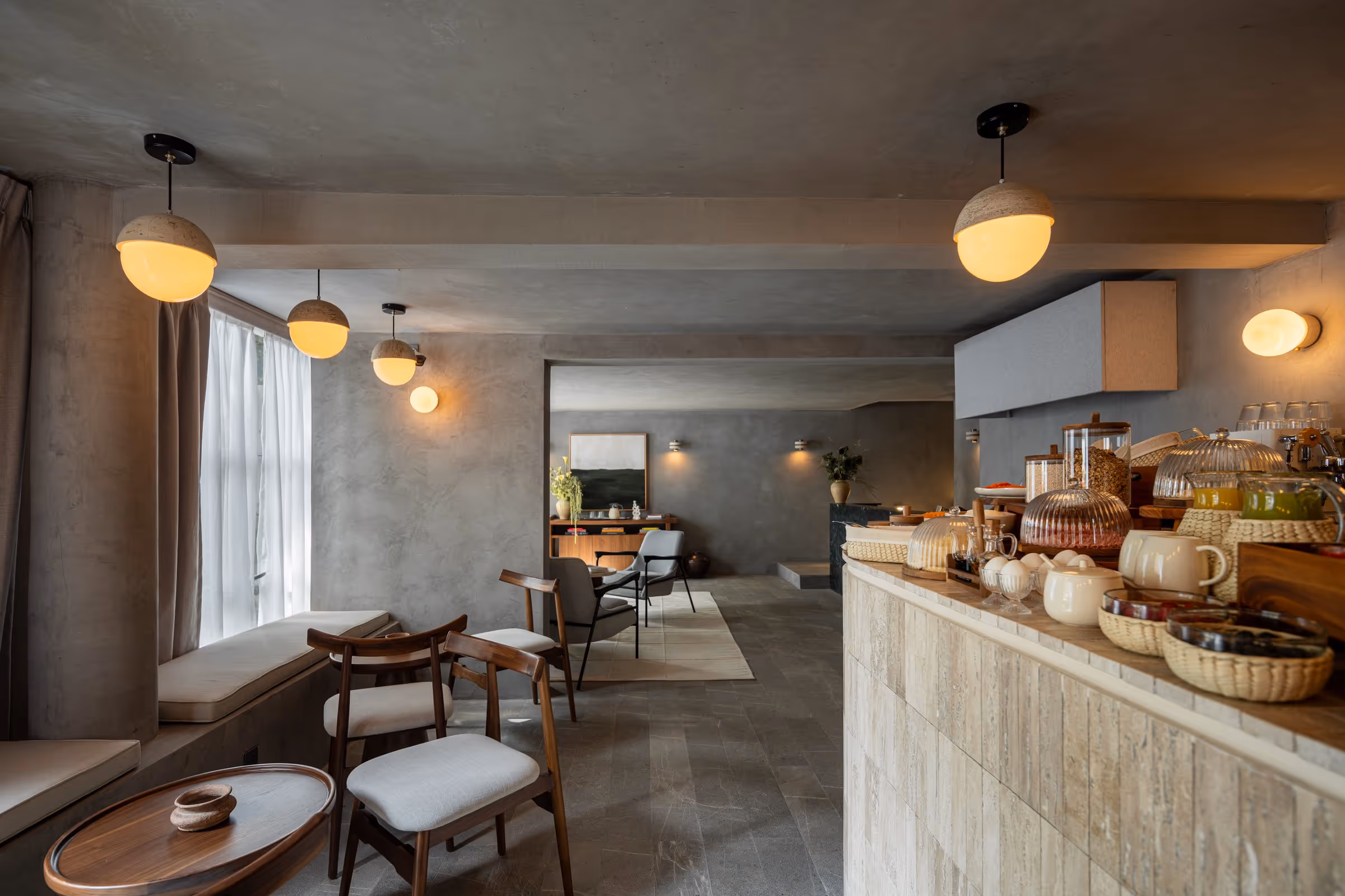 Modern breakfast nook with pendant lights, wooden chairs, cushioned bench, and counter with breakfast items.