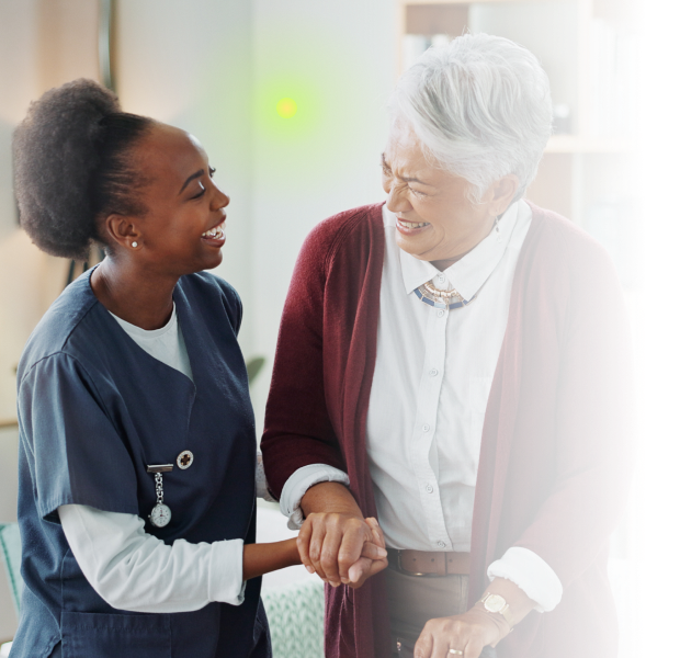 Healthcare worker and elderly woman smiling and holding hands in a warm, supportive interaction.