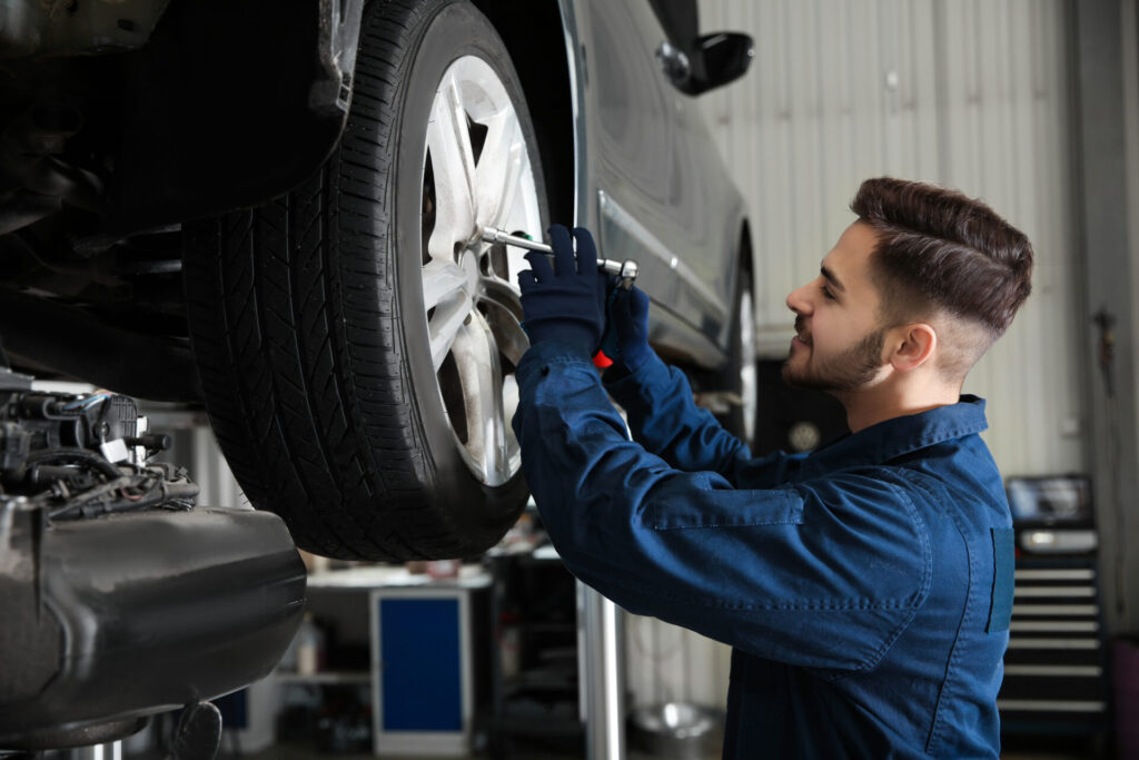 Mechanic in blue coveralls tightening a lug nut on a car wheel in a garage.