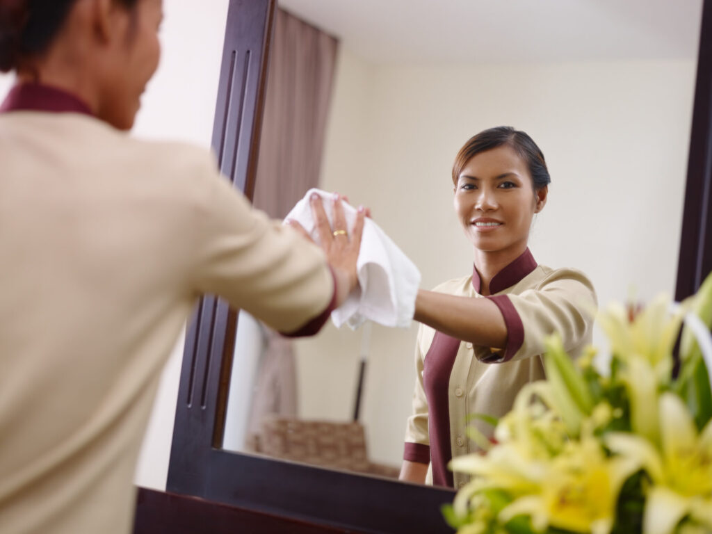 Woman cleaning a mirror with a white cloth while looking at her reflection and smiling.