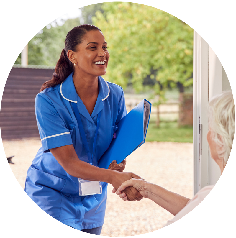 Nurse in blue uniform smiling and shaking hands with an elderly person at a doorway.