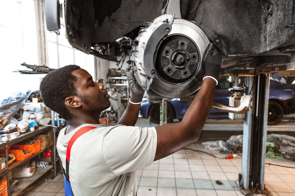 Mechanic inspecting a car's brake disc and caliper in an auto repair shop.