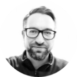 Grayscale image of a man with a beard and glasses smiling slightly.