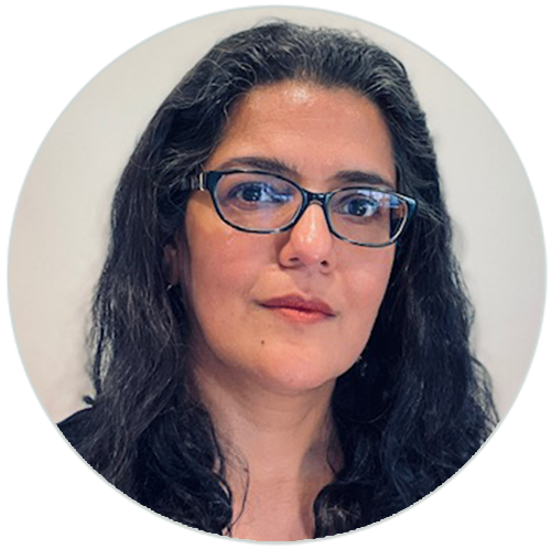 Portrait of a woman with long dark hair, wearing glasses and a black top, against a light background.