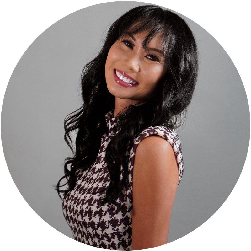 Smiling woman with long black hair wearing a sleeveless patterned dress against a gray background.