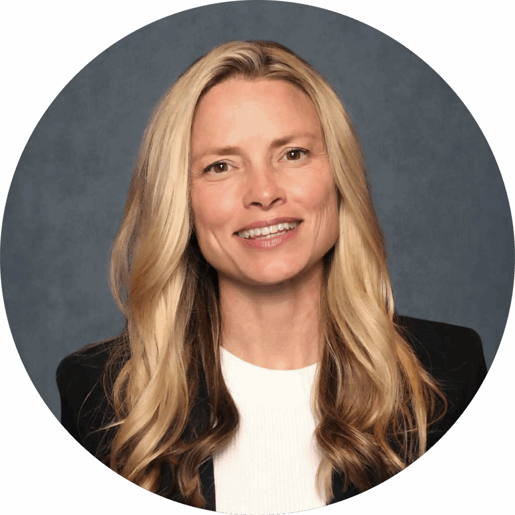 Smiling woman with long blond hair wearing a black blazer and white top against a blue background.