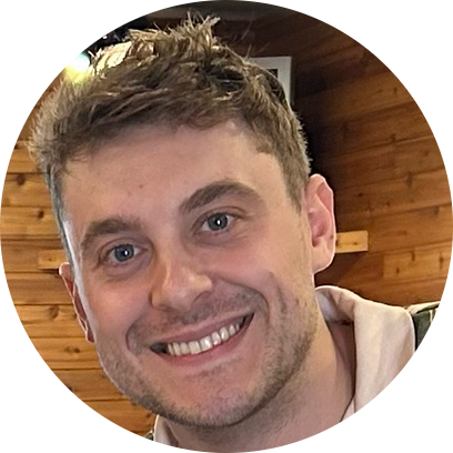 Smiling young man with short light brown hair in a wooden interior.