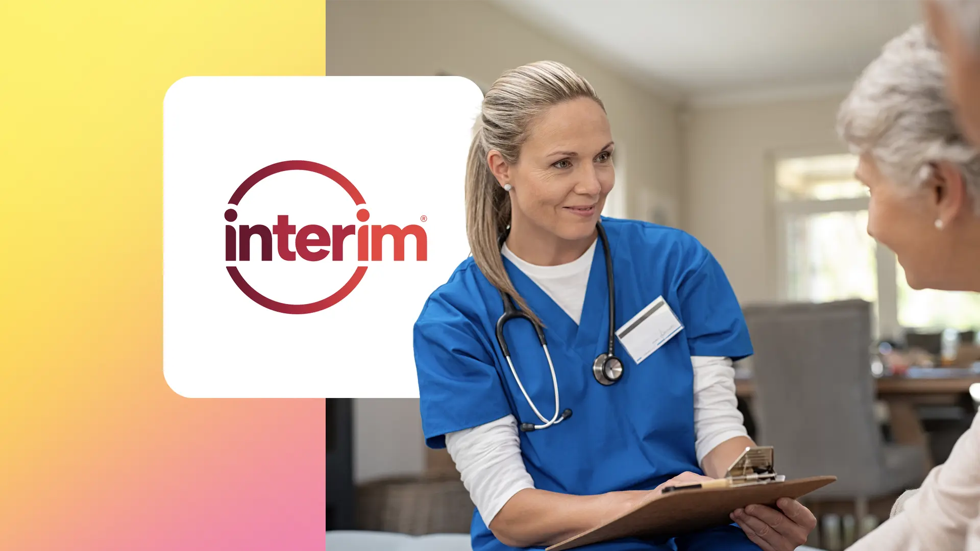 A nurse in blue scrubs with a stethoscope smiles while holding a clipboard and talking to a patient.