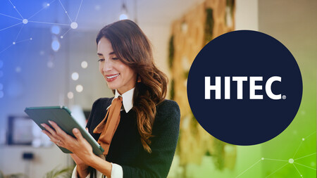 Smiling woman using a tablet with a HITEC logo on a blurred office background.