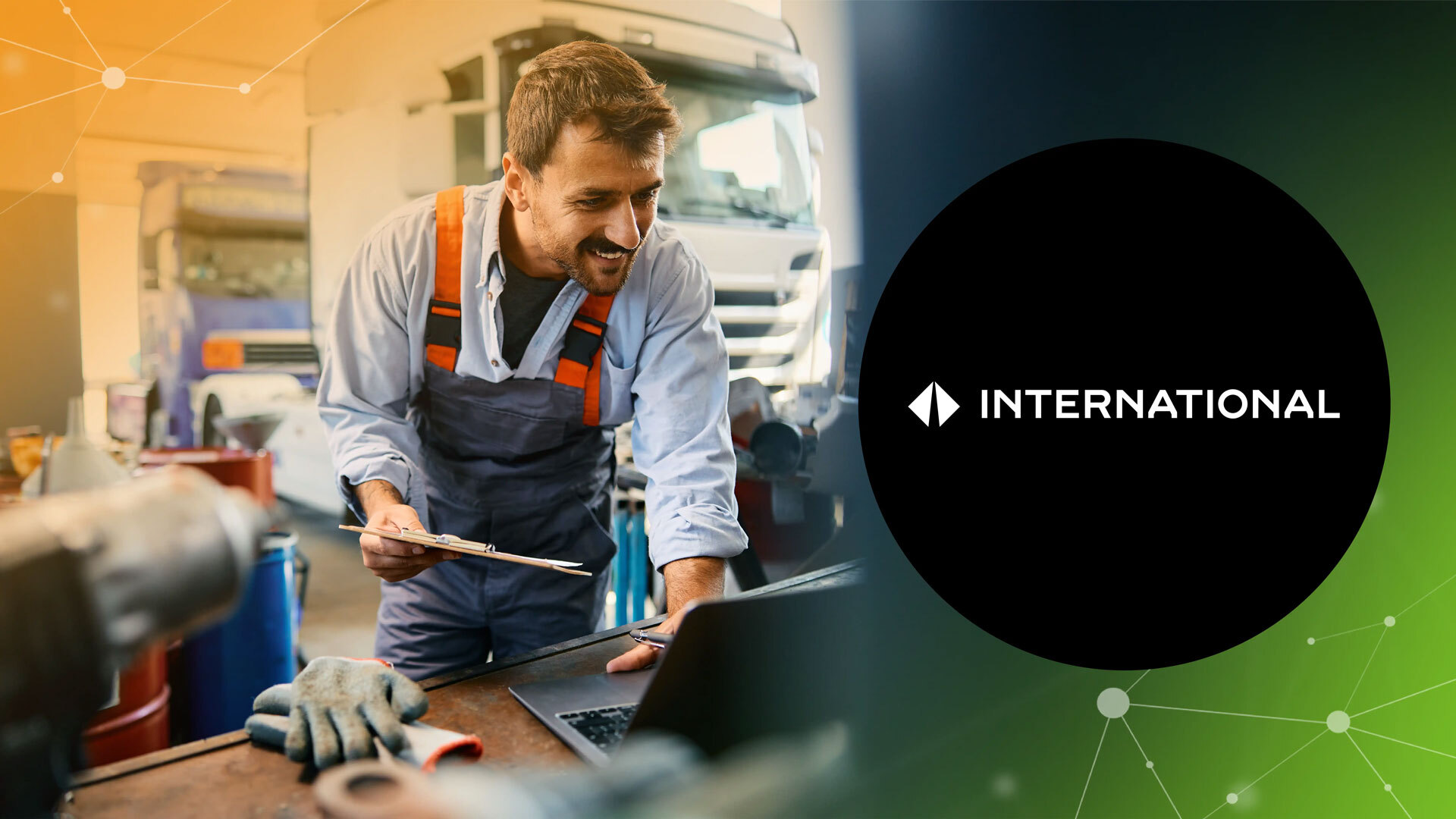 Mechanic in overalls checking a laptop with truck in background in a garage.