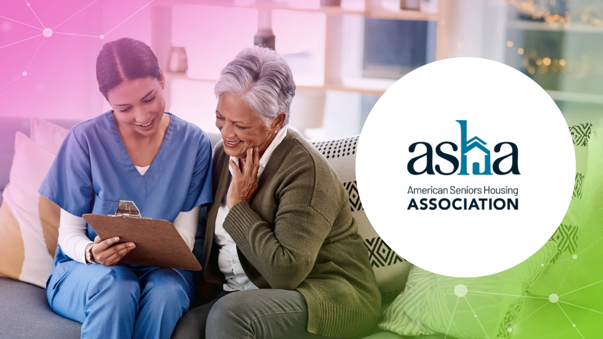 Nurse in blue scrubs with clipboard talking to smiling elderly woman on couch with ASHA logo.