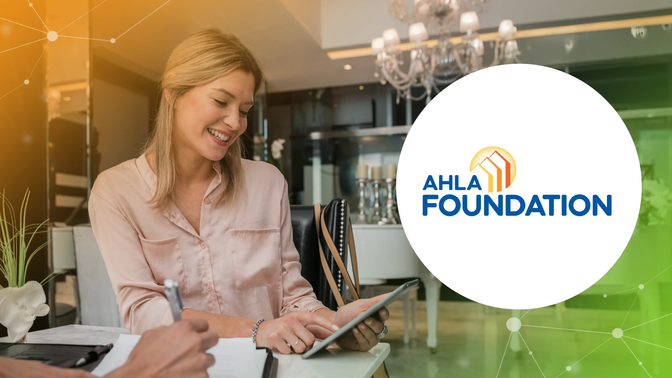Smiling woman using a tablet at a table indoors with AHLA Foundation logo on a white circle overlay.