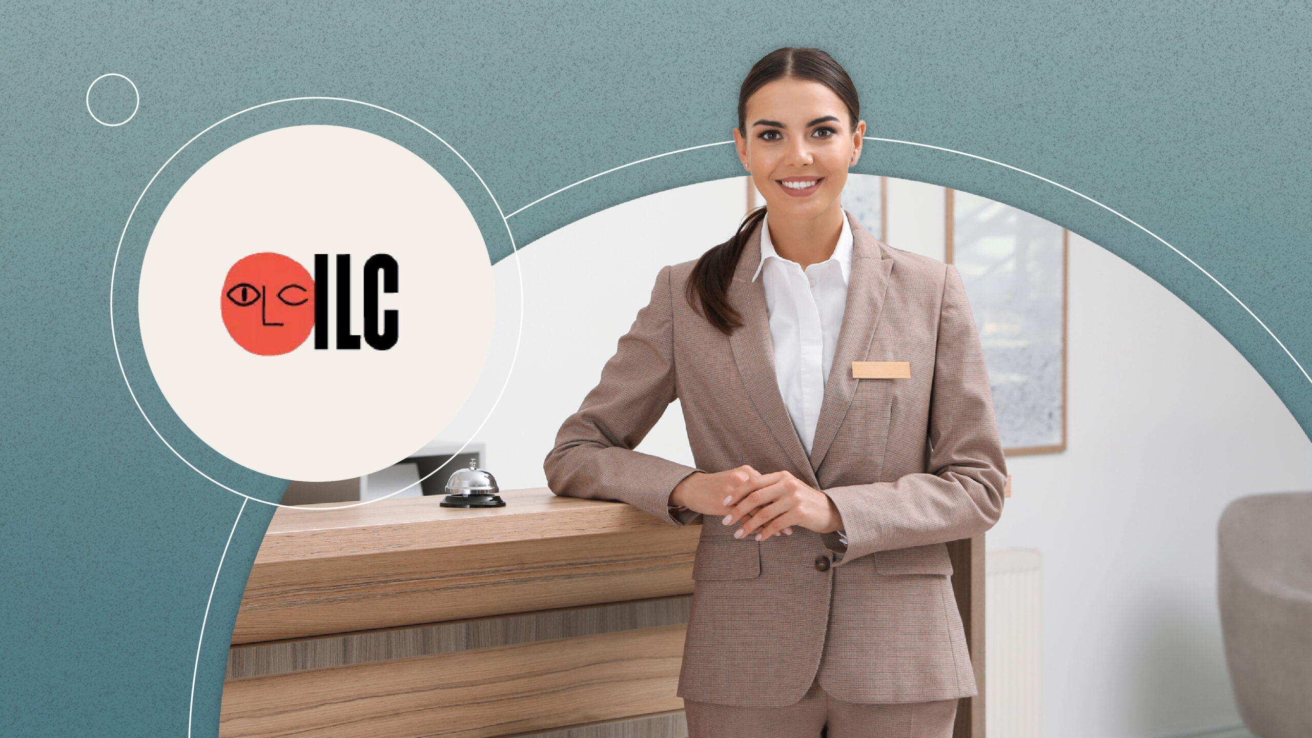 Smiling hotel receptionist in brown suit standing at wooden front desk with service bell.