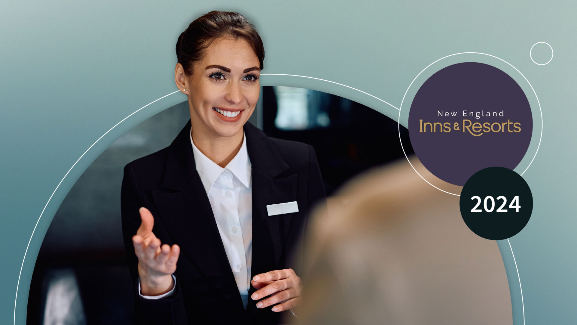 Smiling hotel receptionist in black suit welcoming a guest at front desk.