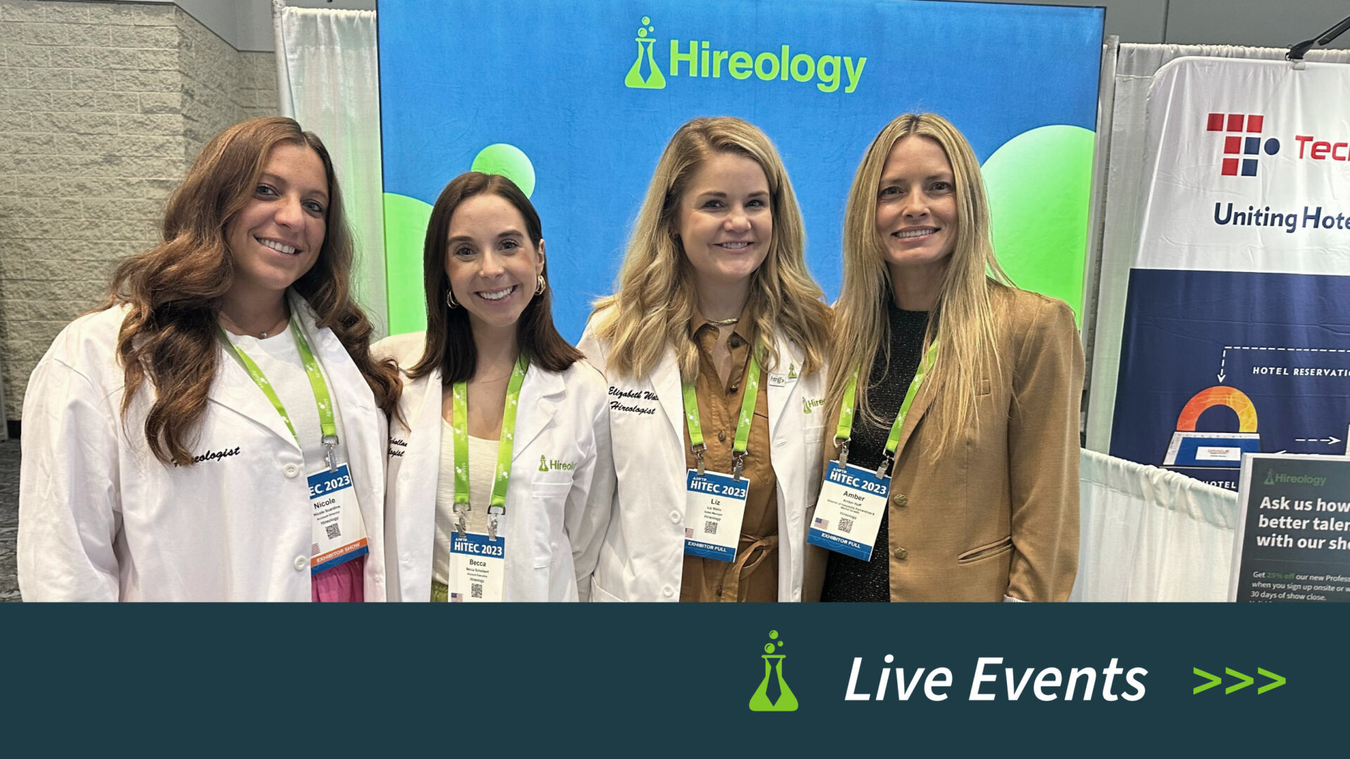 Four women smiling and wearing Hireology badges and white coats or business attire at a conference booth.