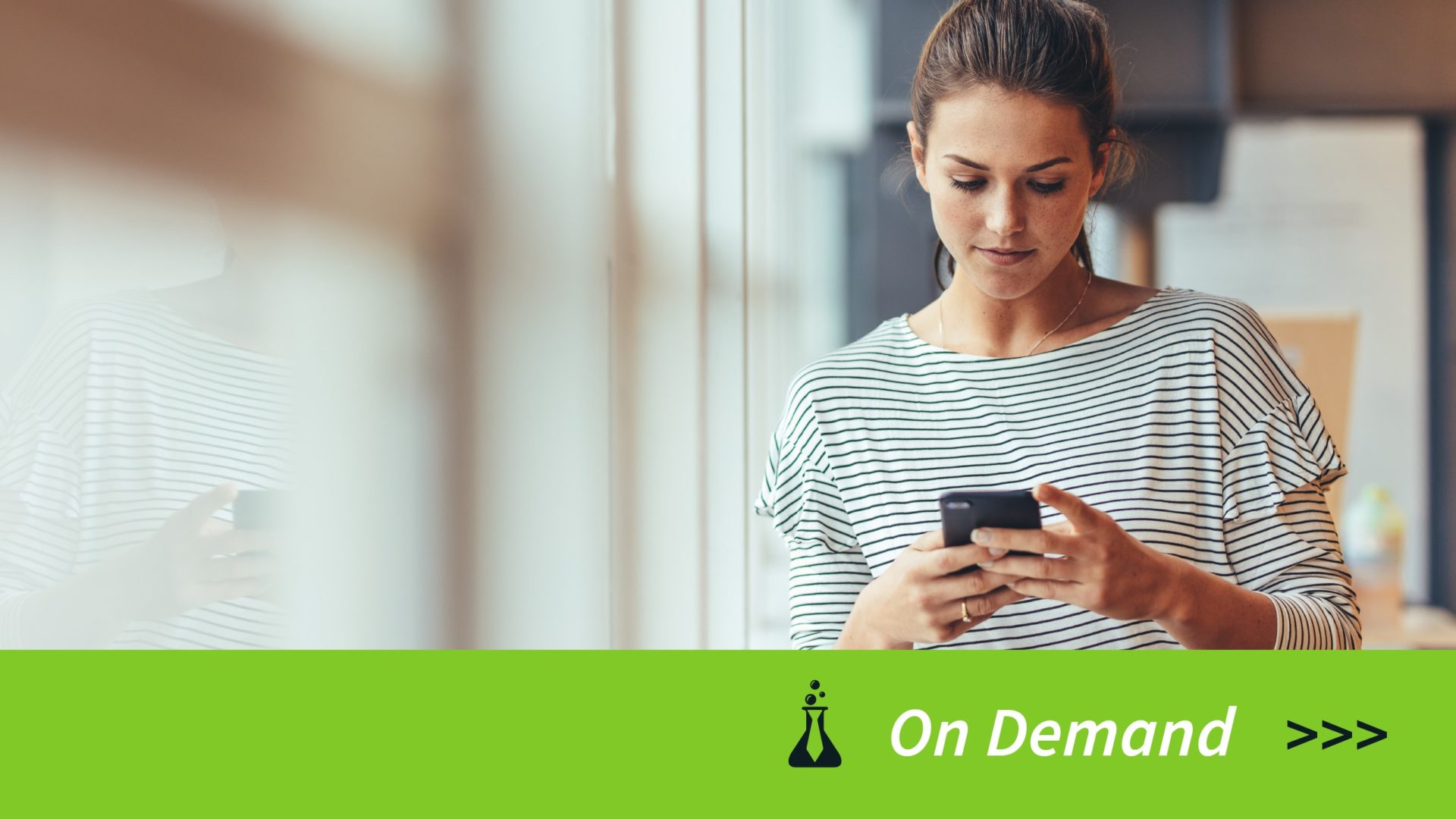 Woman in striped shirt looking down at smartphone with green banner and On Demand text below.