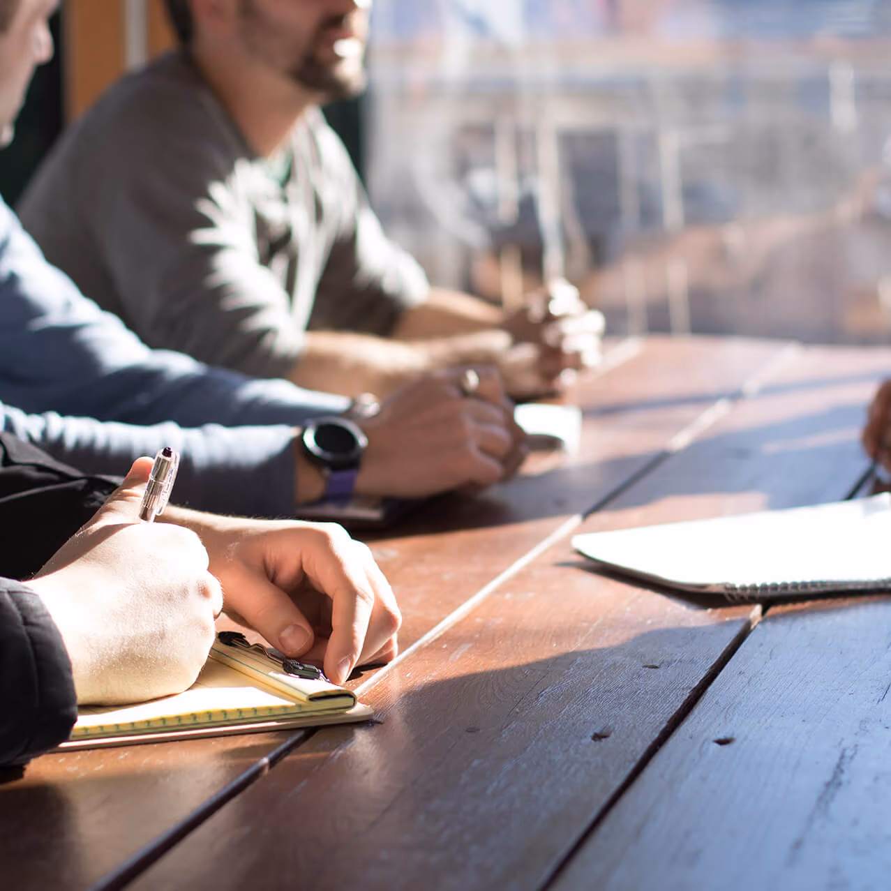 4 people sitting at a desk with paper and pens