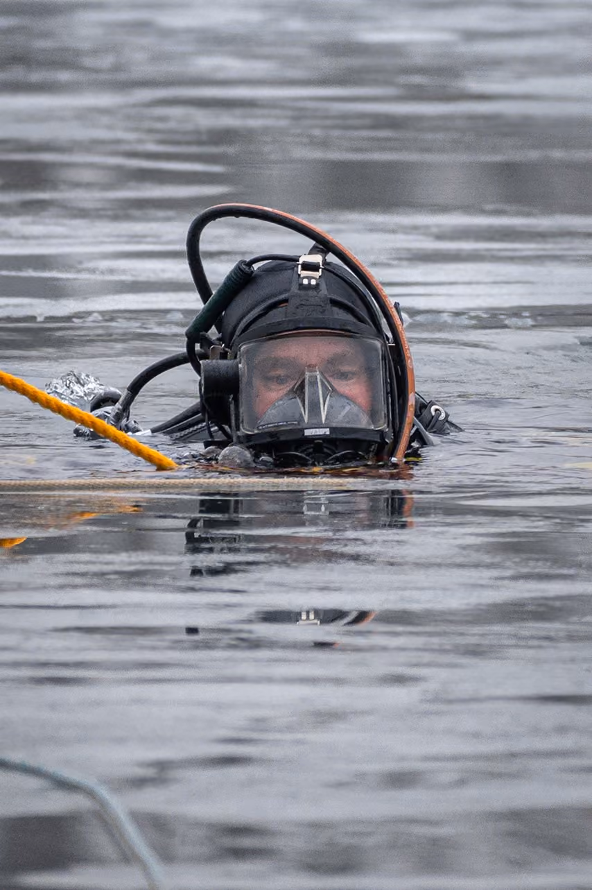 Diver wearing a black full-face mask floats on water surface with an orange safety line.