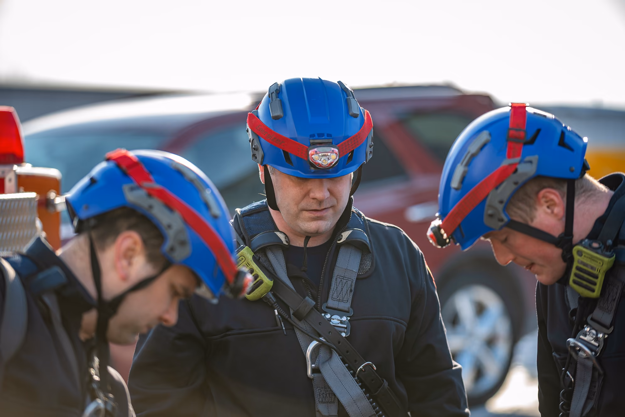 Three rescue workers in blue helmets with headlamps wearing safety harnesses and radios.