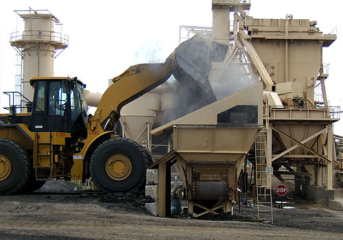 Front loader operating at a construction material processing site with visible dust exposure risk