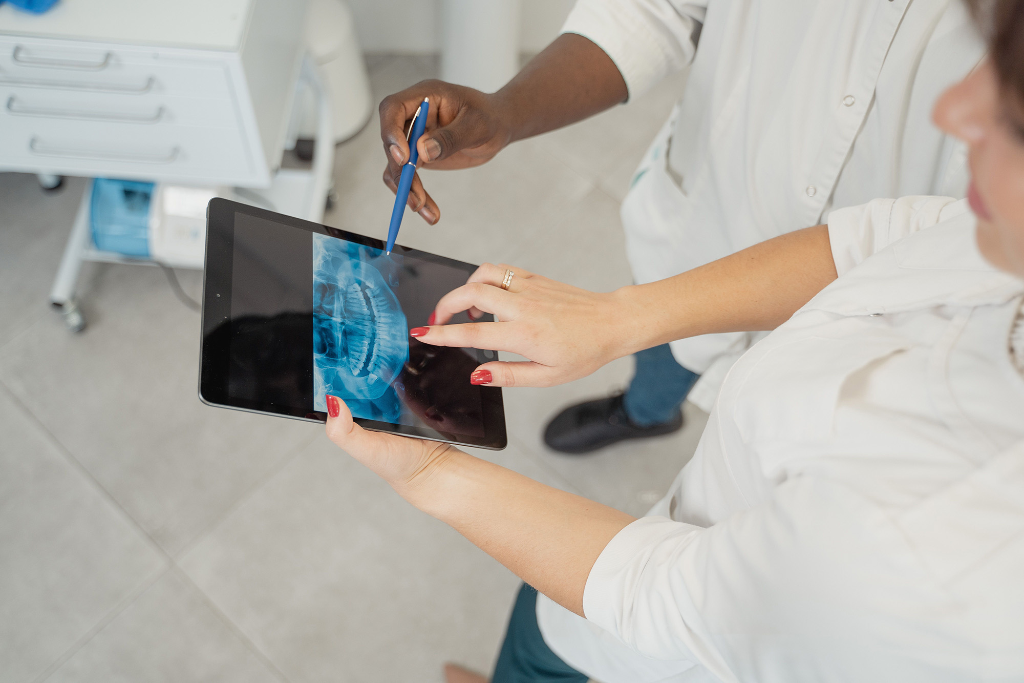 Two dental professionals examining a dental X-ray on a tablet in a clinic setting.