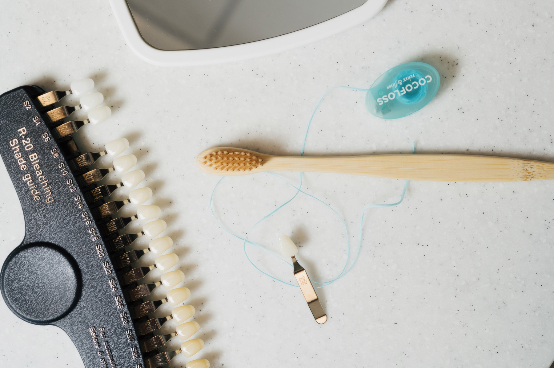 Dental shade guide with bleach shades, bamboo toothbrush, and dental floss on speckled surface.