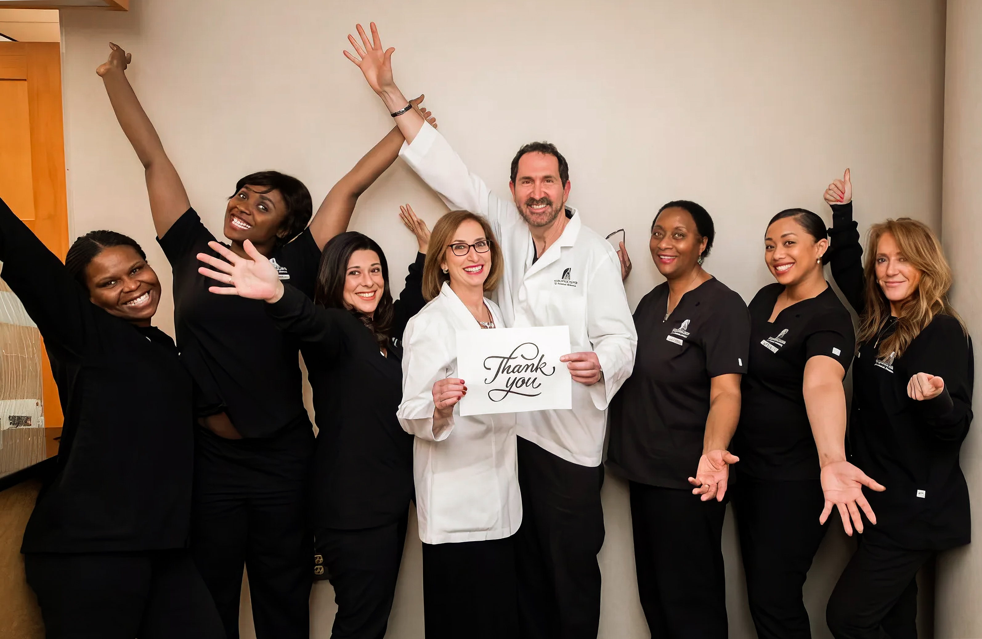 Smiling medical team with two doctors holding a thank you sign, others cheerfully posing around them.