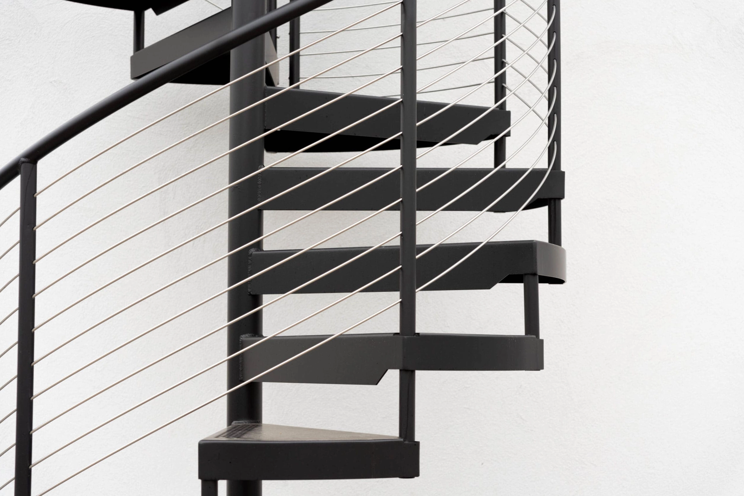 Black spiral stair with cable infill set against a bright exterior wall