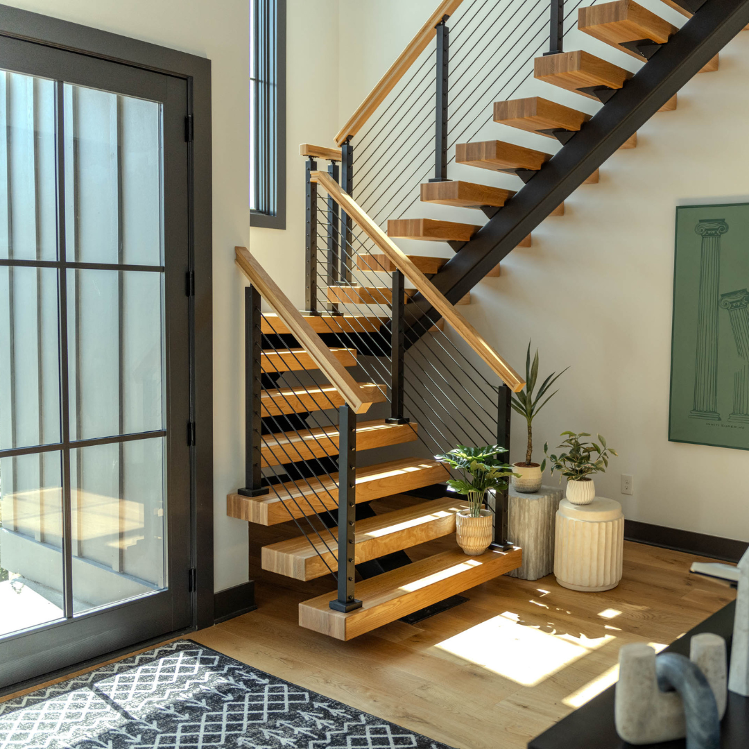 Wood treads and rod infill climb beside a sunlit window and potted plants